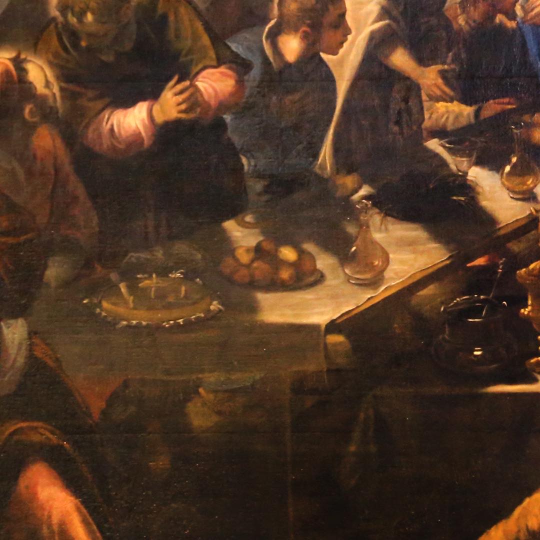 The end of the table: loaves on a pewter plate, a glass decanter, a white cloth.